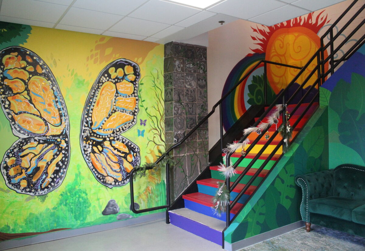 Interior view of murals painted on the wals and staircase of giant butterfly wings, rainbow, sun and jungle leaves within the entrance ans staircase of the InterSrts Center
