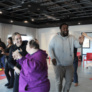 Students in a dance class hold hands with their partners and dance while smiling.