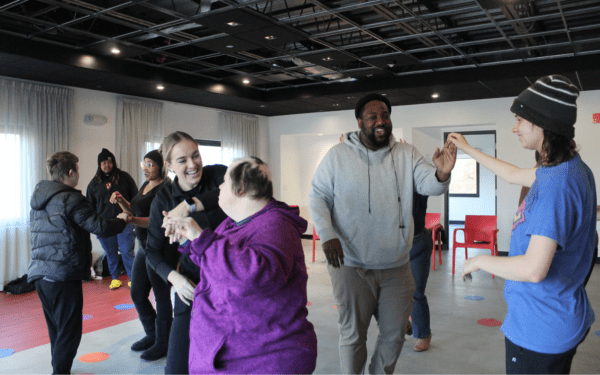 Students in a dance class hold hands with their partners and dance while smiling.