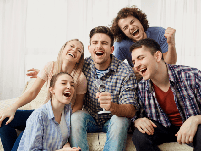 A group of male and female friends singing into a microphone while sitting together on a couch.