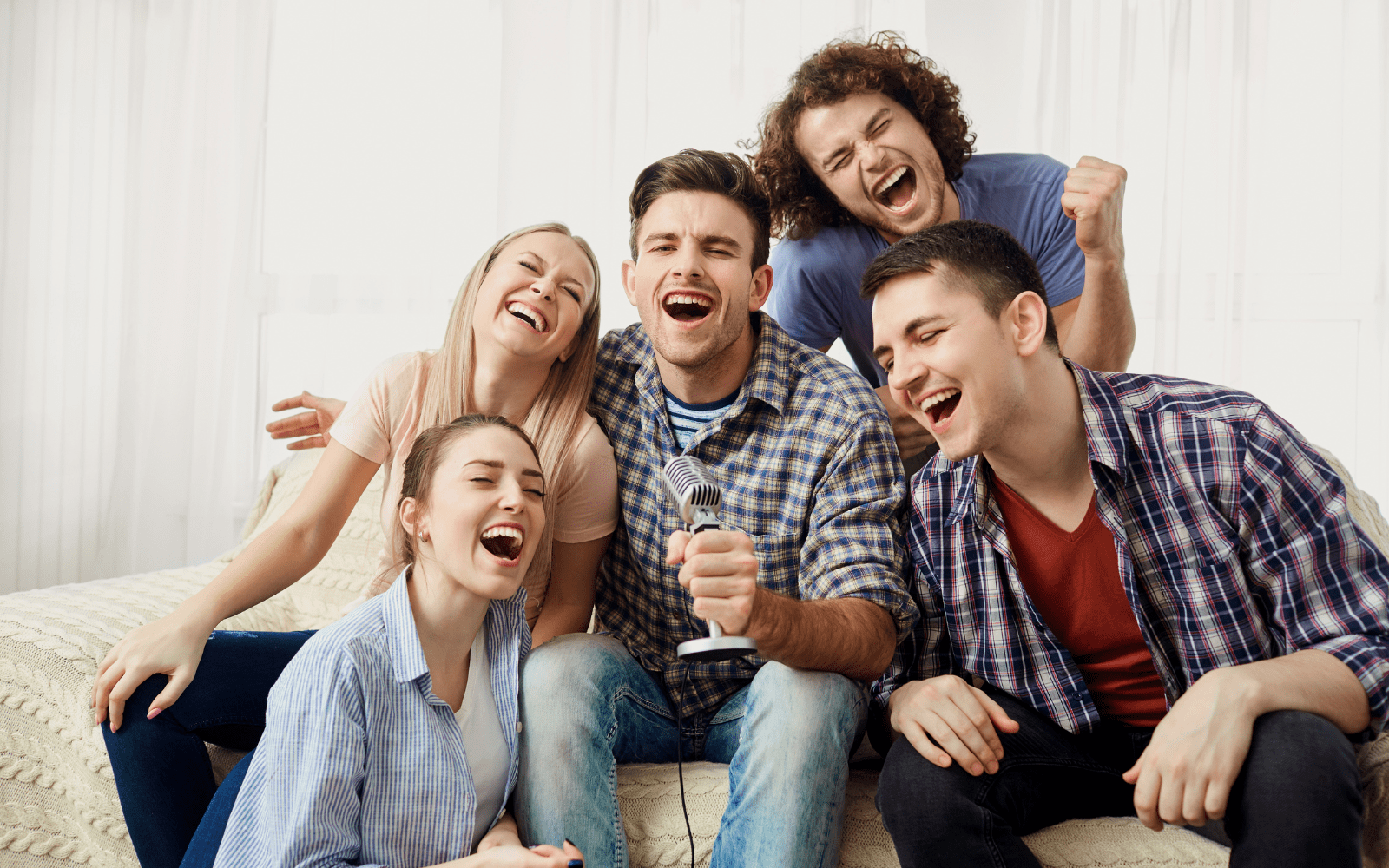 A group of male and female friends singing into a microphone while sitting together on a couch.