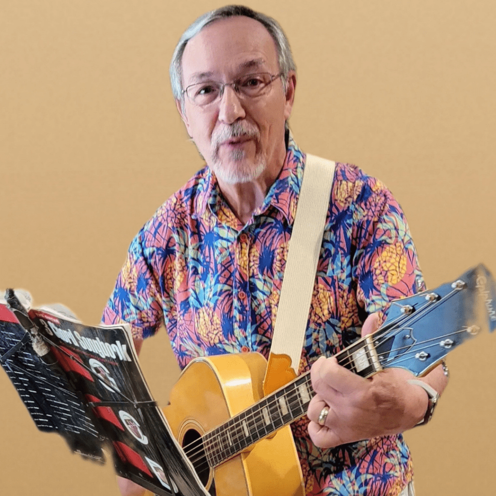 Jeff Greenfield, playing acoustic guitar by a music stand, instructor of music at Hudson Valley InterArts