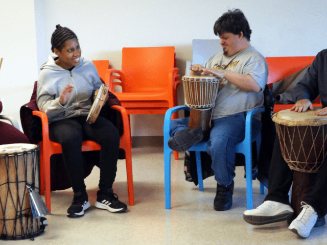 A diverse group of adults sit in colorful chairs and play a variety of drums and rhythm instruments at Hudson Valley InterArts.