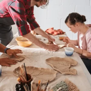 students sit in a ceramics class and with with their hands to shape clay pots