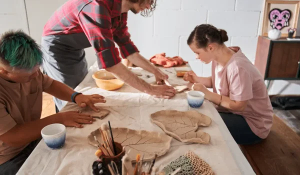 students sit in a ceramics class and with with their hands to shape clay pots