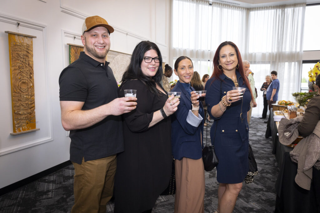 Guests hold up their drinks in the gallery of the Hudson Valley InterArts Center. Wood Carved art by Eric Archer C. Dahlberg hangs on the walls.