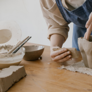 a person forms a clay pot by hand with various tools and a slab of clay on the table.