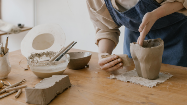 a person forms a clay pot by hand with various tools and a slab of clay on the table.