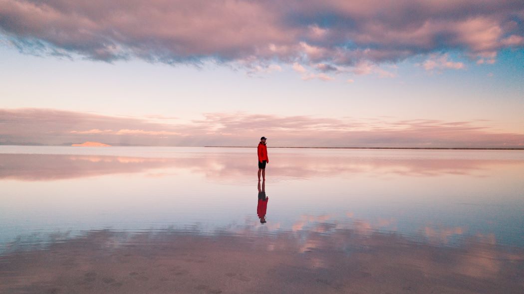 a person standing alone on a lake with clouds