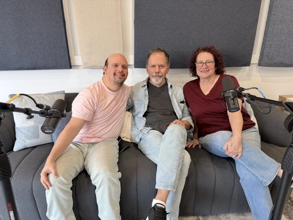 Brandon and his parents Mike and Cathy sitting together on a couch in the StoryWoven recording studio, smiling, with microphones on either side.