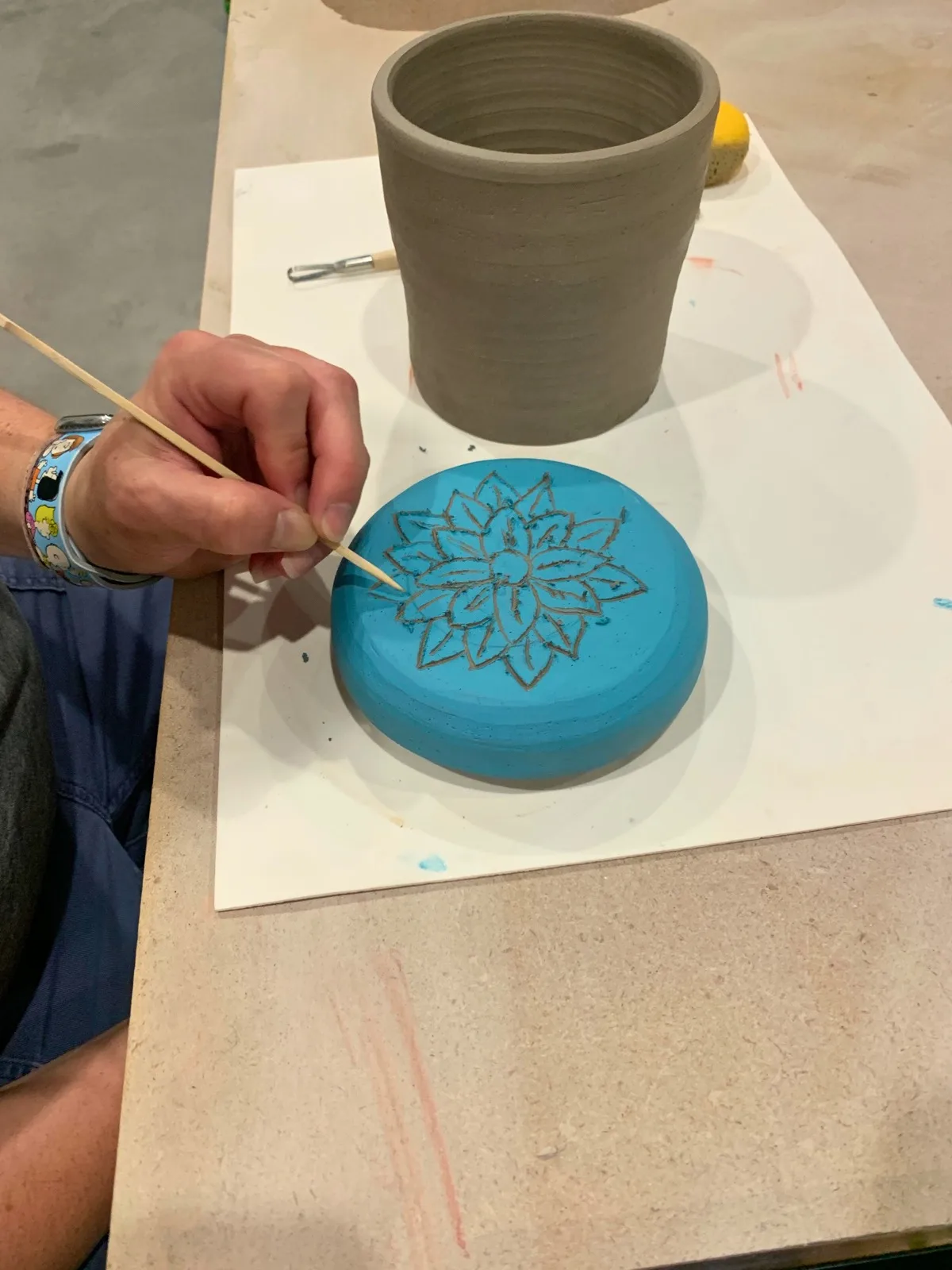 A student carves a floral design into a blue-glazed ceramic lid in an InterArts ceramics class