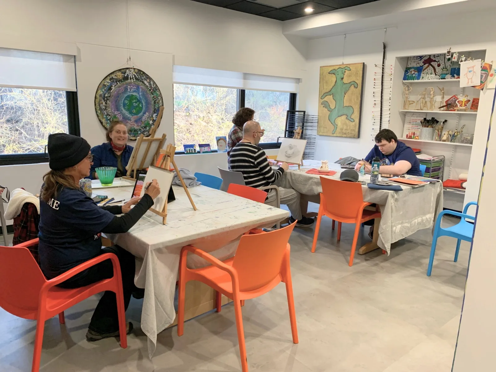 Adults drawing at easels around a table in the bright InterArts art studio