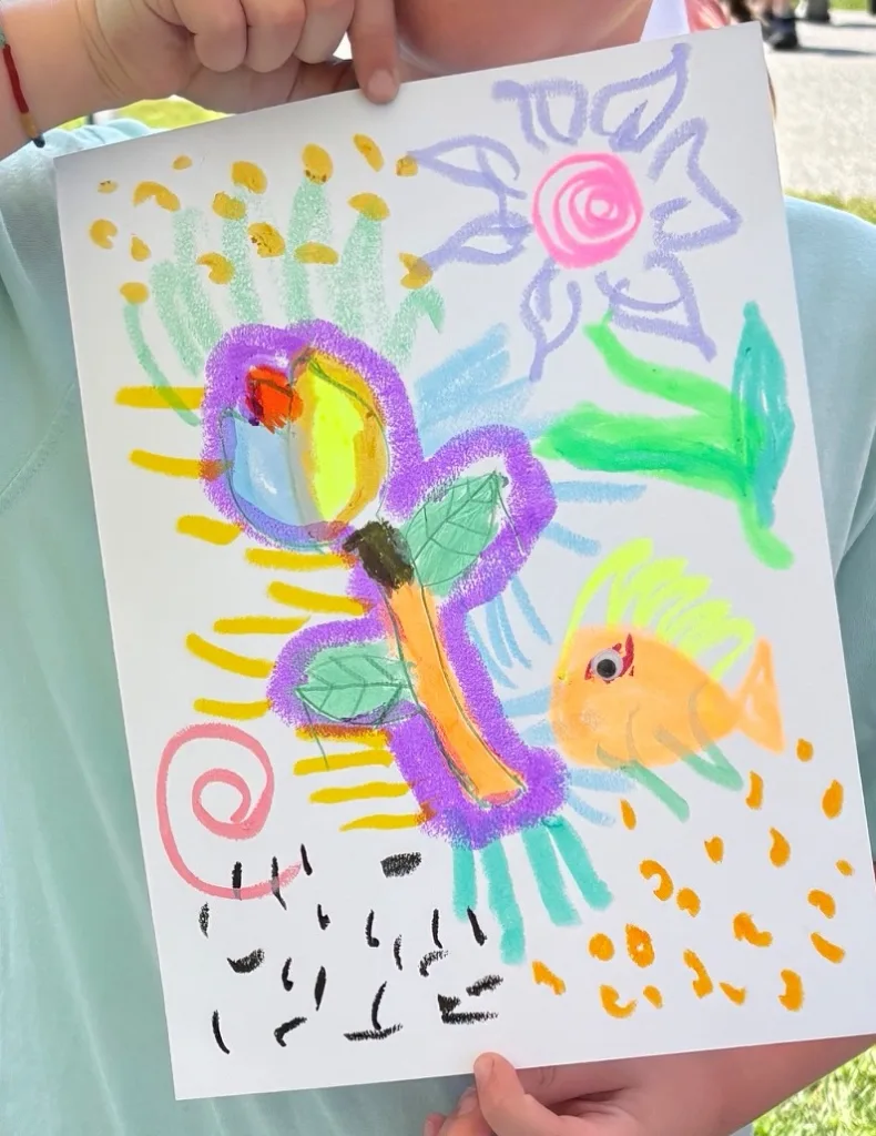 A child's oil pastel drawing of a purple butterfly, an orange fish and a pink flower, made at the InterArts booth at the Putnam County Fair.
