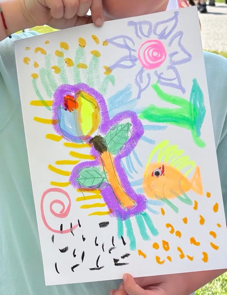 A child's oil pastel drawing of a purple butterfly, an orange fish and a pink flower, made at the InterArts booth at the Putnam County Fair.