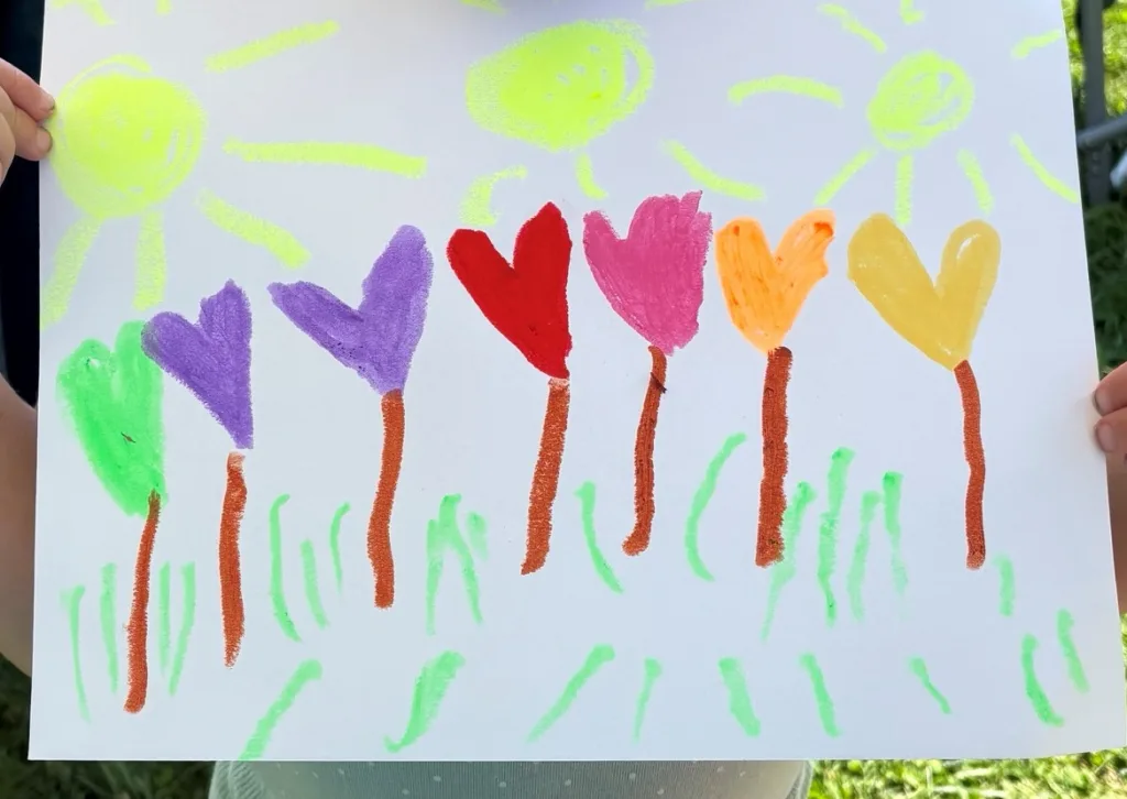 A child's drawing of six heart-shaped flowers under three yellow suns, made at the InterArts booth at the Putnam County Fair.