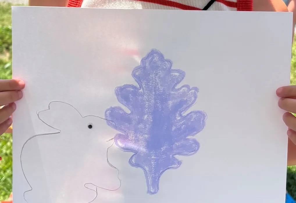 A purple oak-leaf rubbing beside a pencil-drawn creature, made at the InterArts booth at the Putnam County Fair.